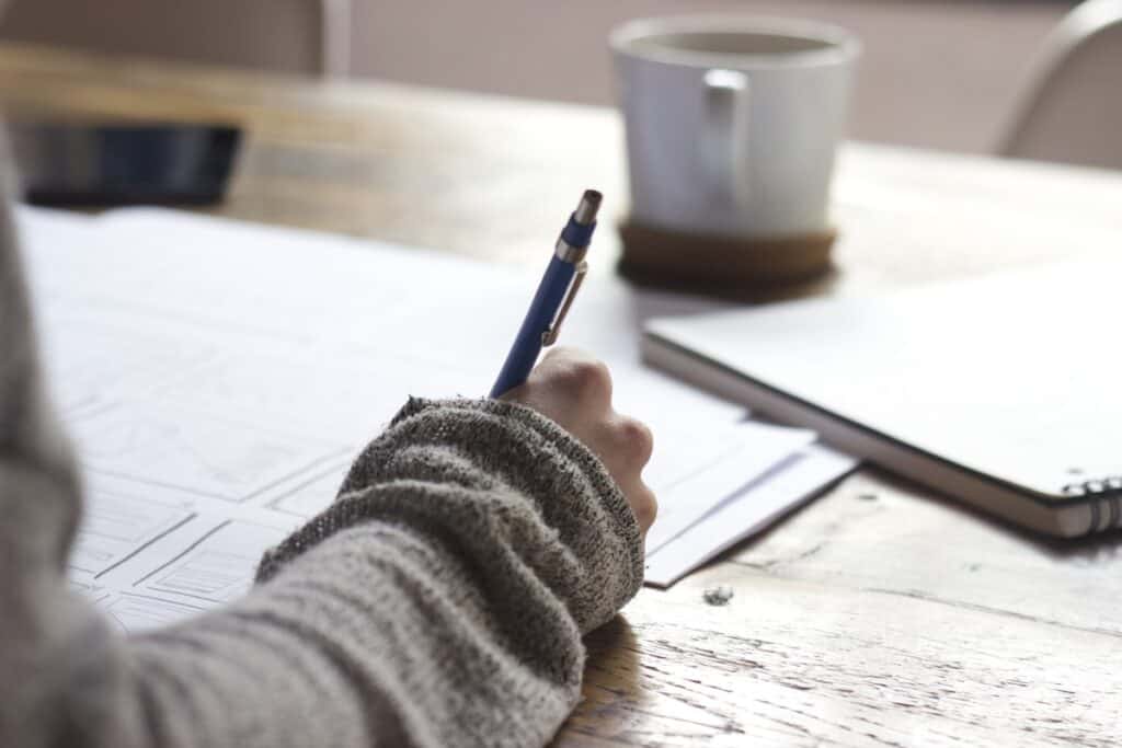 Personne écrivant sur un cahier avec stylo, étude pour Cours NDRC.