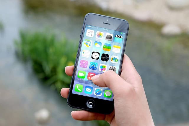 Main d'une personne tenant un smartphone avec applications diverses affichées.